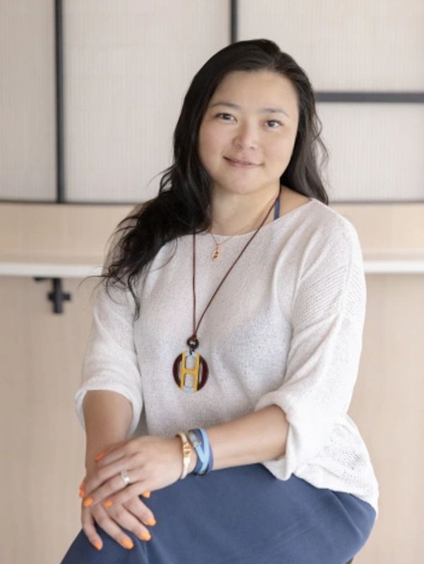 Woman with black hair, wearing white sweater and blue skirt.
