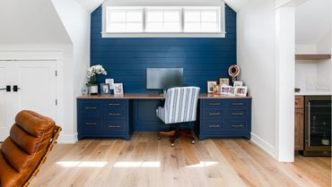 Cozy home office with navy blue cabinets and a striped chair under a large window.