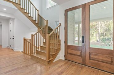 Bright entryway with wooden stairs and large glass-paneled double doors.
