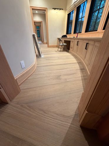A curved wooden floor hallway with a desk, chair, and large windows.