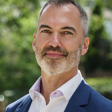 Professional man with gray beard in blue suit jacket outdoors.