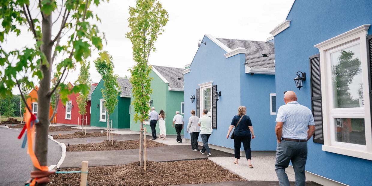 People walking past colorful houses on a street.