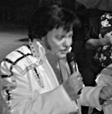 Man in a white embellished jacket singing into a microphone.