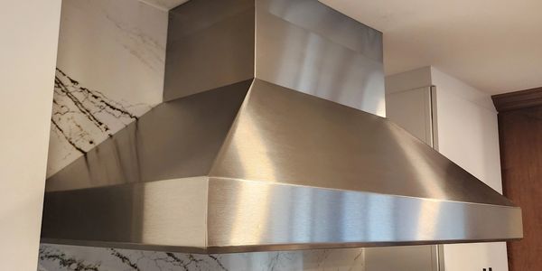 Modern stainless steel kitchen range hood with marble backsplash.