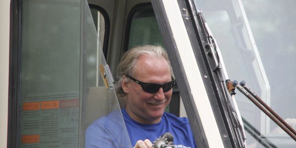 Man wearing sunglasses operating machinery inside a cabin.