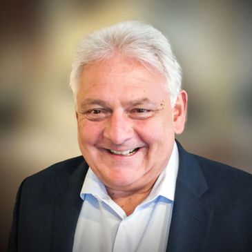 Smiling elderly man with white hair in a suit jacket.