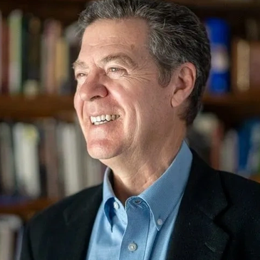 Smiling man in a blue shirt and black blazer, looking sideways.