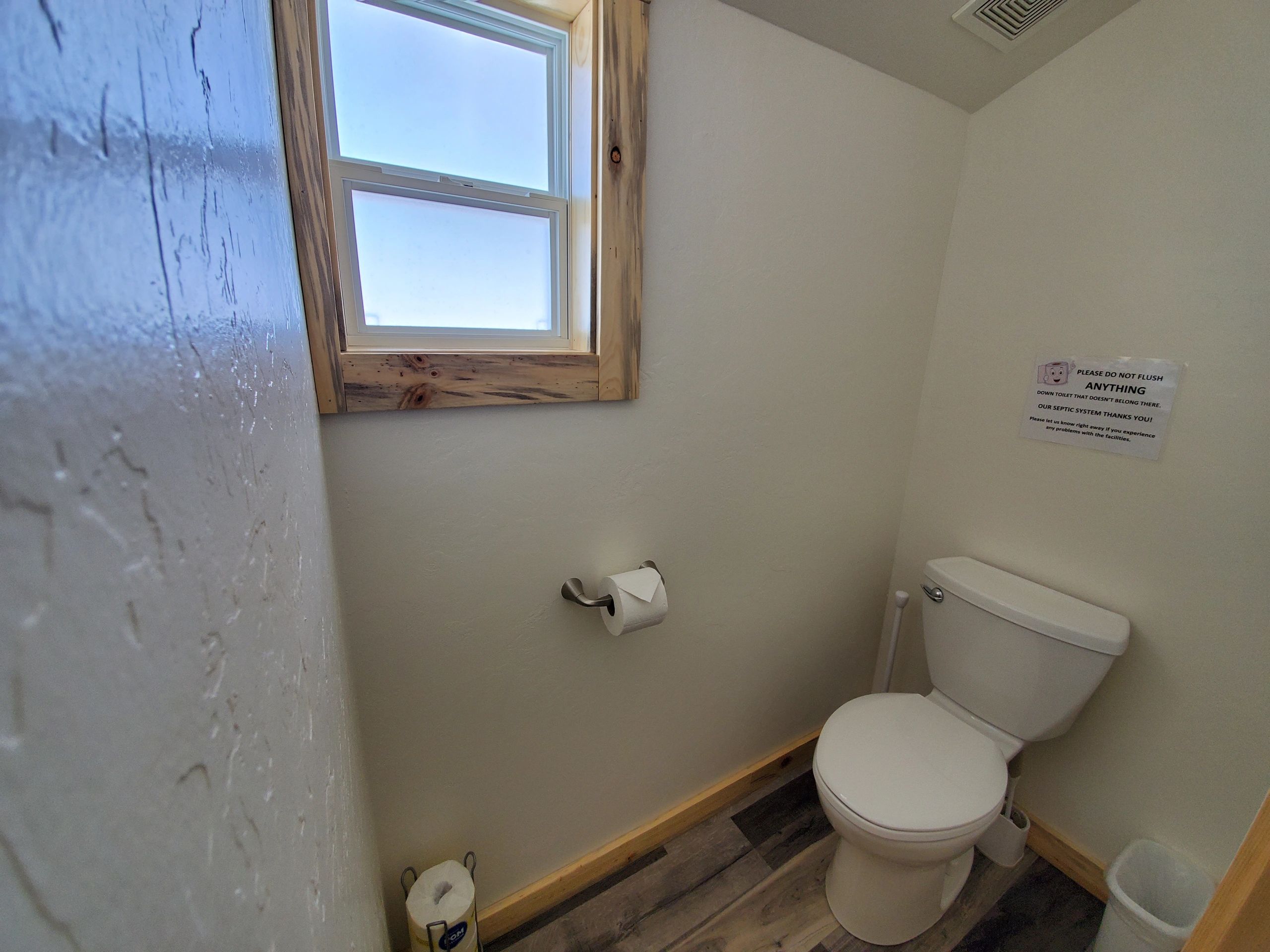 A bathroom with a toilet, window, and wooden floor