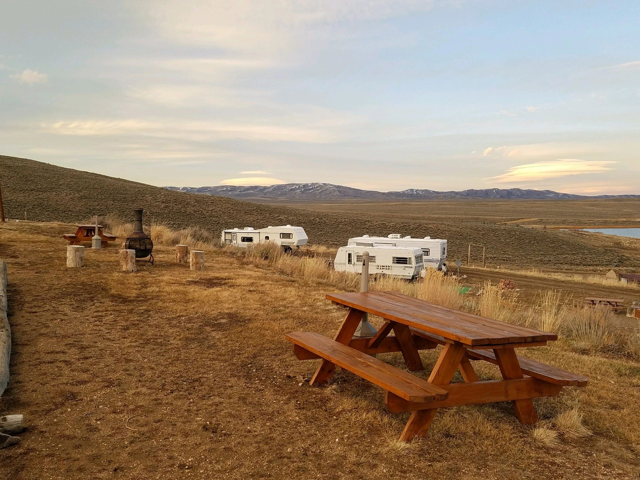 A wide view of a grassy hillside with picnic tables, campers, and a mountain range in the background.