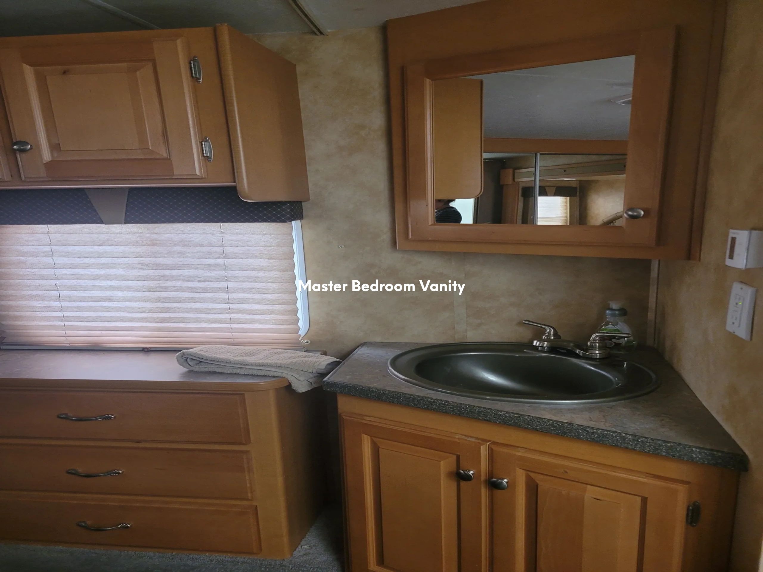 A bathroom vanity with wood cabinets, a stone countertop, and a metal sink under a mirror.