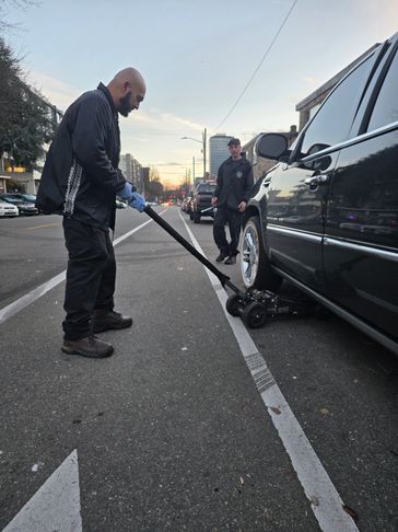 A man uses a jack to lift a black car on the street.