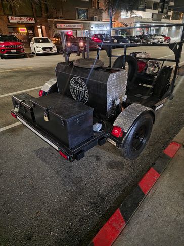 A custom-built trailer with a metal tank and storage box parked on the street at night.