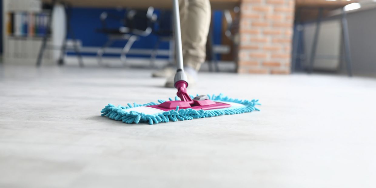 Close-up of a person mopping a floor with a blue mop indoors.