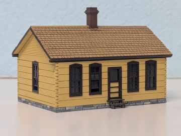 A miniature yellow house model with black windows and a chimney.