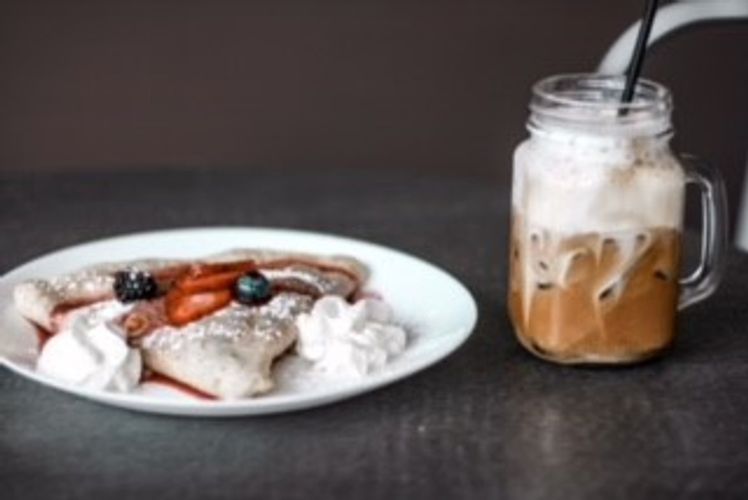 plate of crepes with whipped creme beside a mug of shaken cold coffee