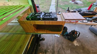 Custom wooden kitchenette with a gas stove and cutting board extension.