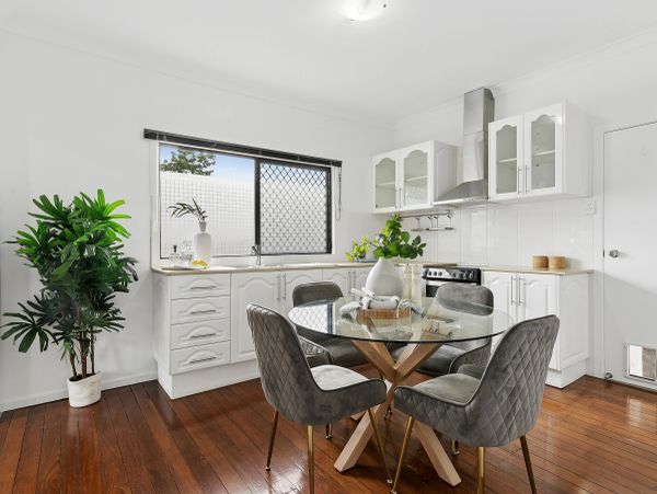 Modern white kitchen with glass dining table and grey chairs.