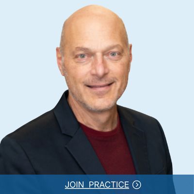 Professional portrait of a smiling bald man in a dark blazer and maroon shirt.