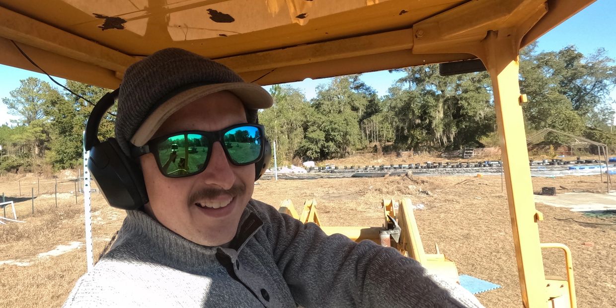 Man wearing sunglasses and headphones smiling inside a yellow construction vehicle.