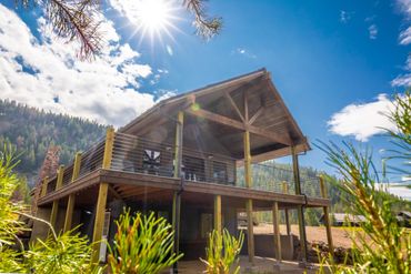 A wooden cabin with a large deck under a bright sun and blue sky.