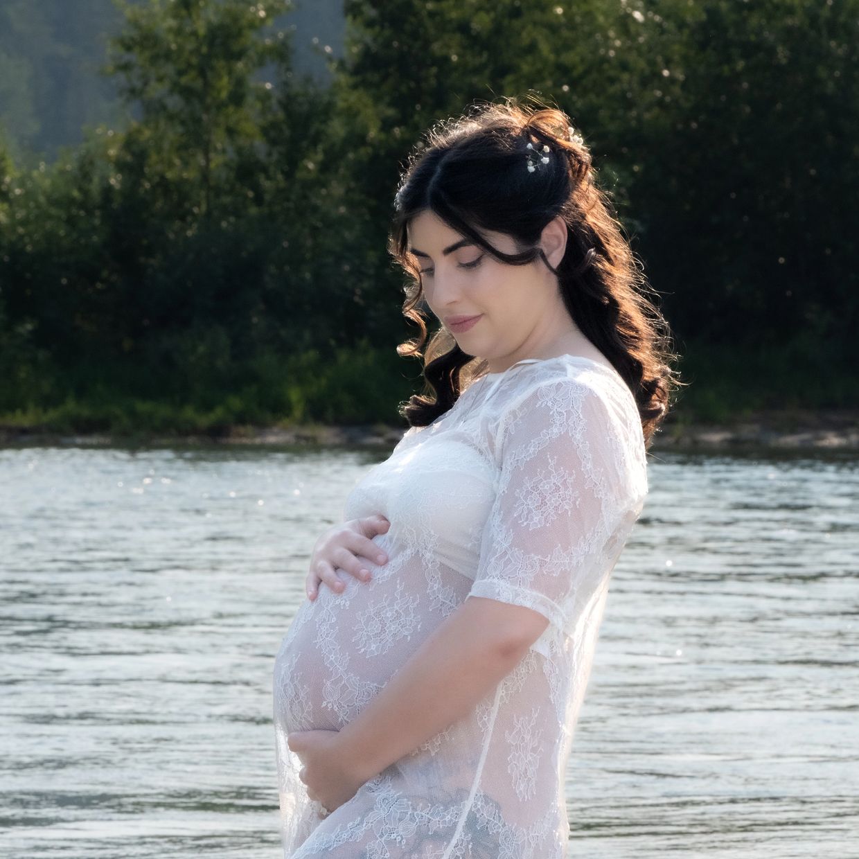 Pregnant woman in a white lace dress by the water.