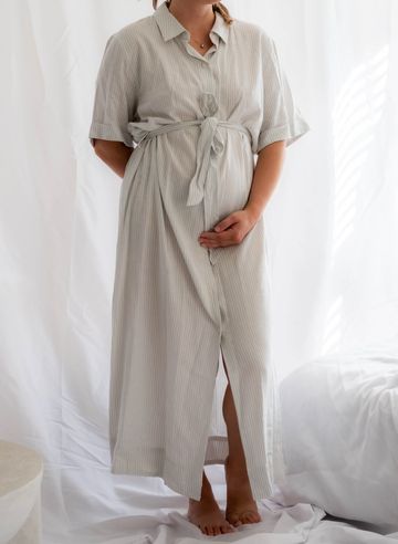 Pregnant woman in a light dress holding her belly.