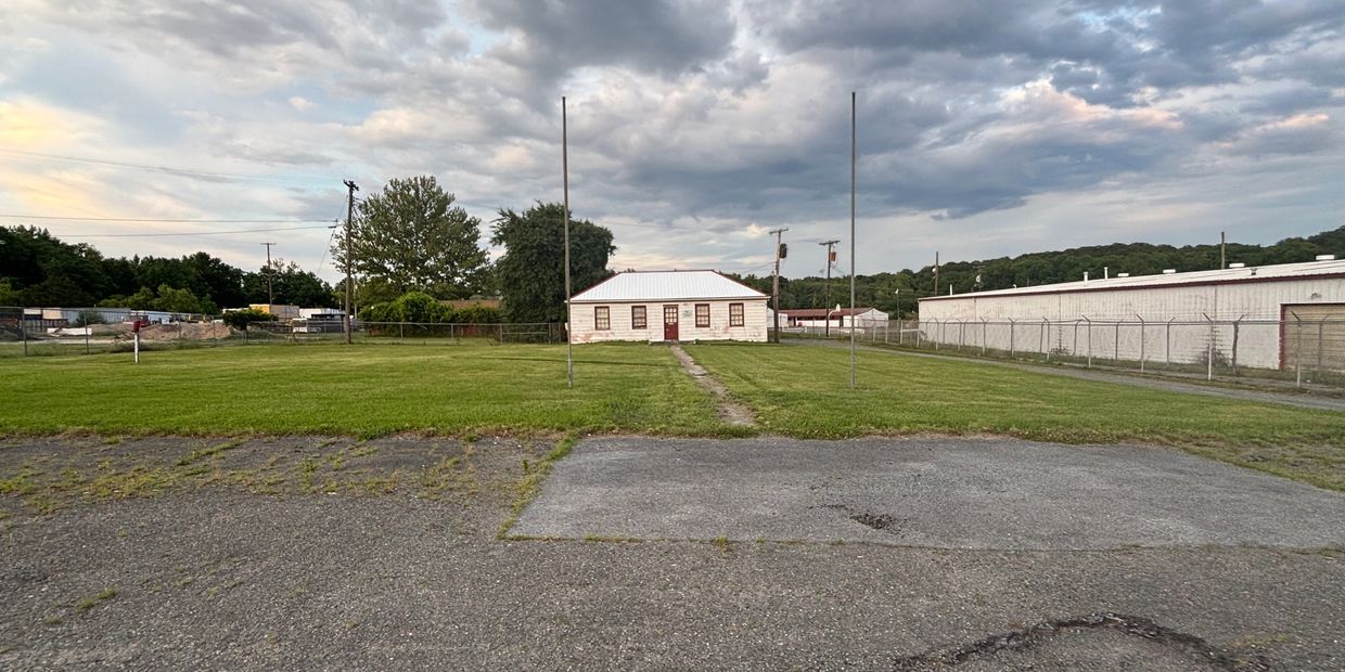 Small white house with a metal roof in a large grassy field.