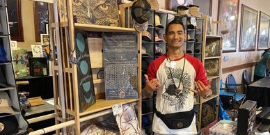 Man smiling at a market stall displaying hats and art.