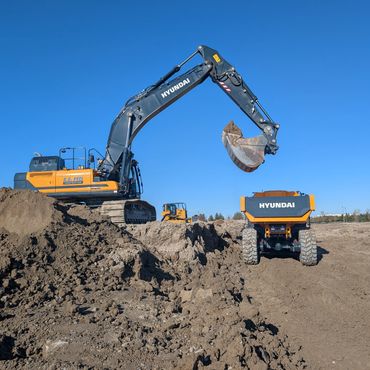 Excavator loading dirt into a dump truck at a construction site under clear blue sky.
