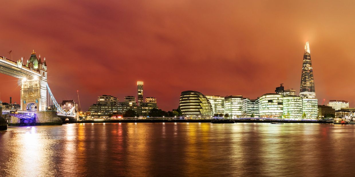 Night view of London skyline with Tower Bridge and The Shard reflecting on the River Thames.