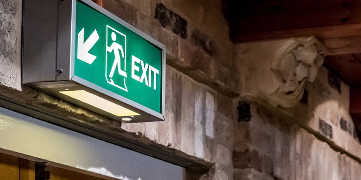 Illuminated green exit sign with a left arrow on a stone wall.