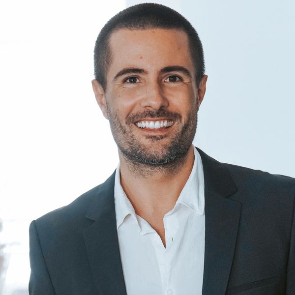 Smiling man in a black suit and white shirt standing indoors.