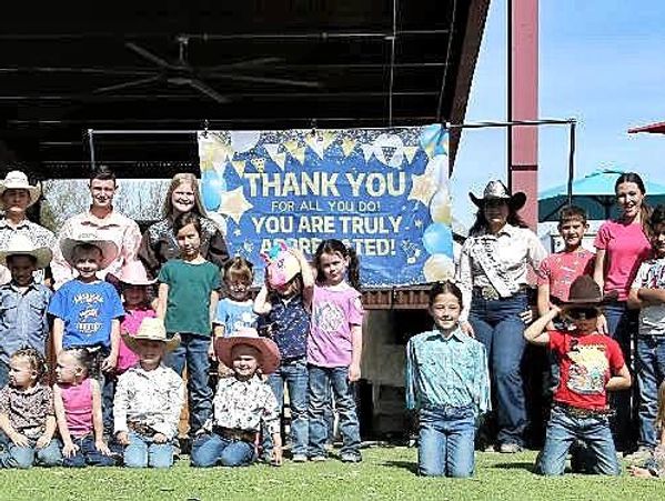 Group of children and adults posing in front of a thank you banner outdoors.