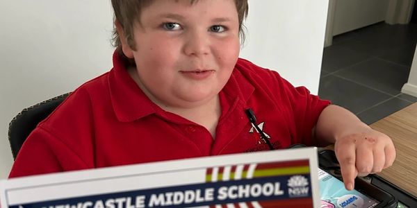 Boy in a red shirt holding a Newcastle Middle School paper.