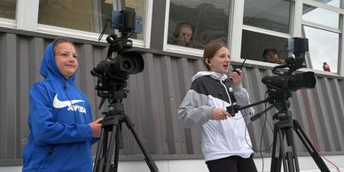 Two teenagers operating video cameras outdoors.