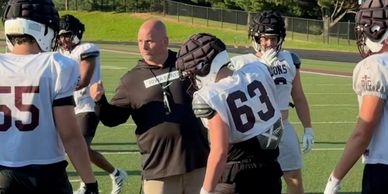 Coach instructing high school football players during practice.