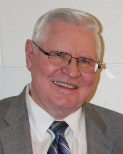 Smiling elderly man in glasses and suit jacket.