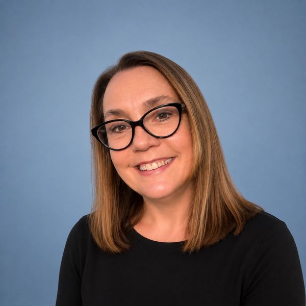 Smiling woman with glasses and shoulder-length hair against a blue background.