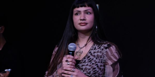 Woman with long dark hair holding a microphone on stage.
