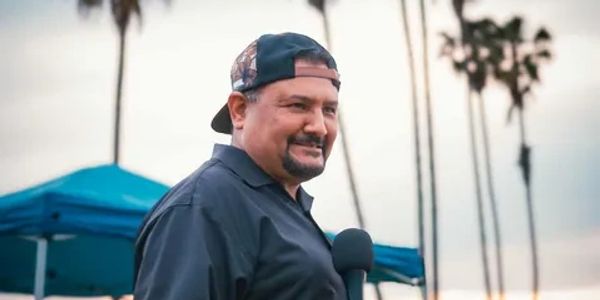 Man in a backwards cap holding a microphone outdoors.