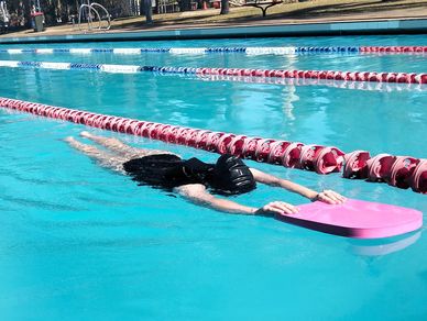 Person swimming with a kickboard in an outdoor pool.