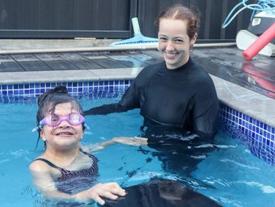 A smiling woman and a girl in a swimming pool, the girl wearing goggles.