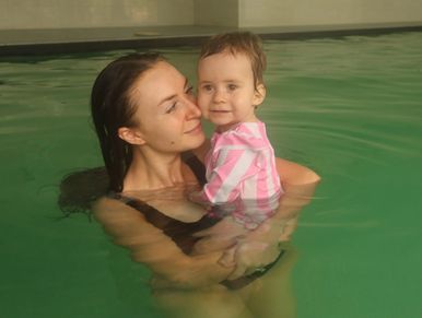 A woman holding a baby in a swimming pool, both smiling gently.