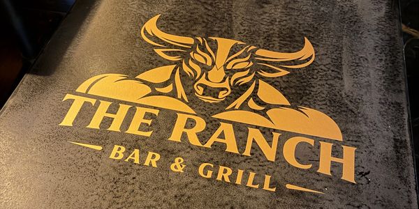 Logo of The Ranch Bar &amp; Grill with a bull's head design on a textured surface.