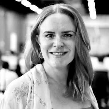 Smiling woman with light hair in a softly lit indoor setting.