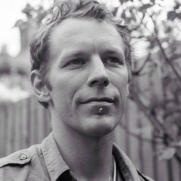 Black and white portrait of a man with a lip piercing outdoors.