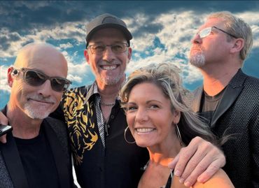 Four adults smiling outdoors under a dramatic cloudy sky.