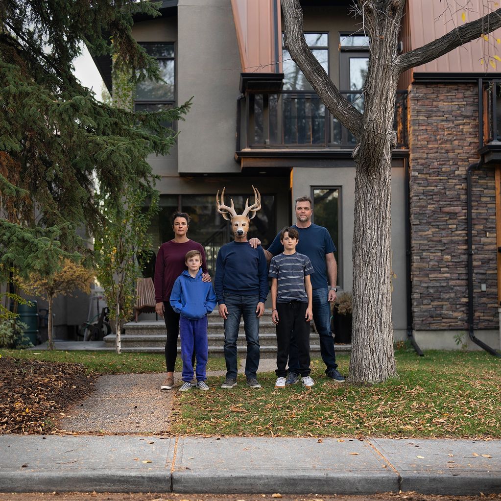 A family poses outside their home, with one member wearing a deer mask.