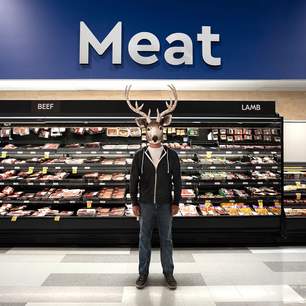 A person with a deer mask stands in the meat aisle of a grocery store.
