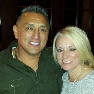 A smiling man and woman posing together against a dark background.